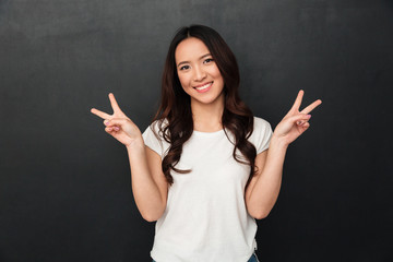 Poster - Pleased asian woman in t-shirt showing peace gestures