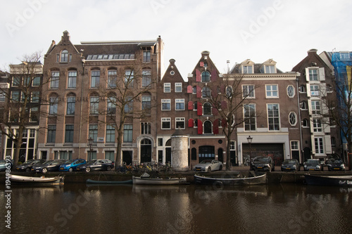 Plakat Wielokolorowe domy w Amsterdamie na głównym kanale miasta. Typowy holenderski holenderski dom z wieloma oknami i pionowo rozwinięty. Łodzie na dole
