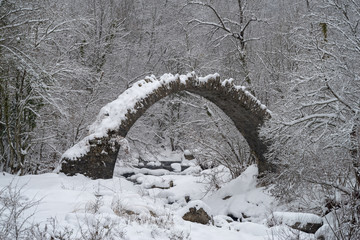 Arch bridge in mountains during winter, South Alps, Italy