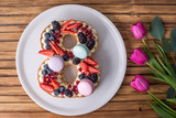 Fototapeta  - Cake in shape of number 8 decorated with berries and flowers tulips. Dessert for women's day on the eighth of March