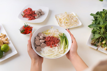 Female chef prepare traditional Vietnamese soup Pho bo with herbs, meat, rice noodles