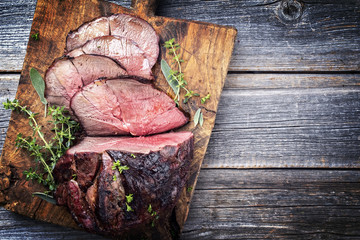 barbecue dry aged haunch of venison with herbs as close-up on an old cutting board