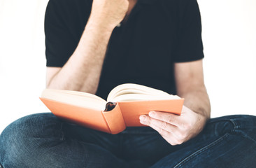 male person in casual clothing sitting cross legged reading a hardcover book