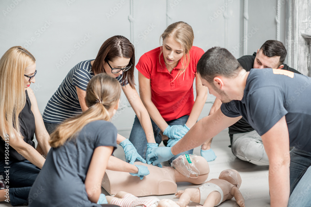 Group of people learning how to make first aid heart compressions with dummies during the training indoors - obrazy, fototapety, plakaty 