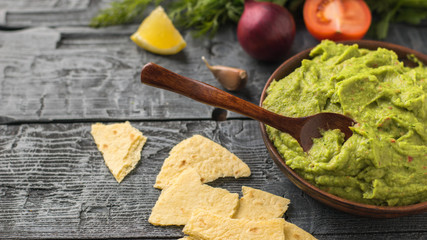 Clay bowl with freshly made guacamole and pieces of Mexican tortilla on a rustic wooden table. Diet vegetarian Mexican food avocado.