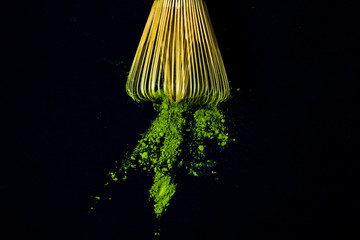 Close up bamboo whisk and matcha green tea powder on black background.