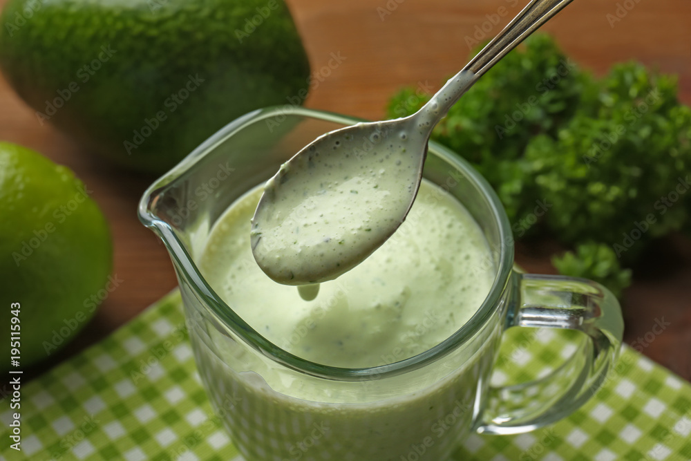 Spoon with creamy avocado lime sauce for fish taco over jug on kitchen table