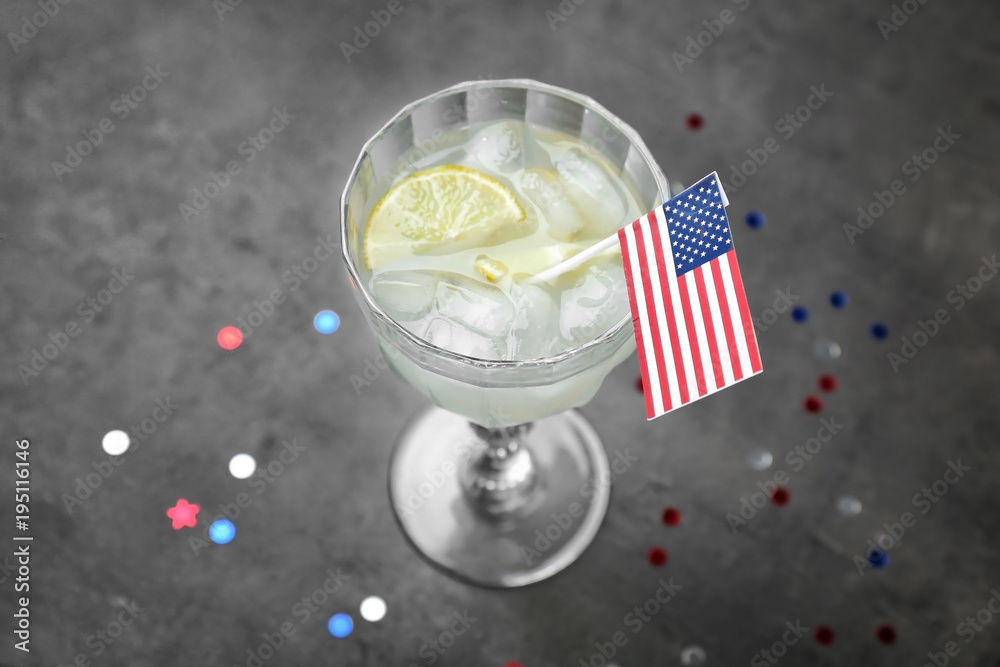 Glass with alcoholic cocktail and small American flag on grey background