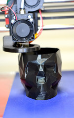 3D printer printing a model in the form of black skull close-up. The 4ht industrial revolution. Automatic three dimensional performs plastic modeling. Progressive modern additive technology