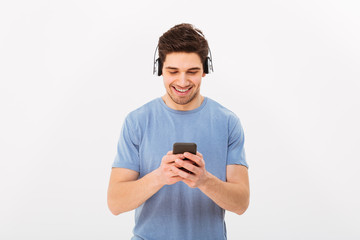 Sticker - Attractive man with short dark hair listening to music via wireless headphones and holding cell phone, isolated over white background