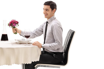 Sticker - Young man seated at a restaurant table holding a bouquet of flowers