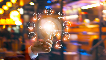 Wall Mural - hand holding light bulb in front of global show the world's consumption with icons energy sources fo