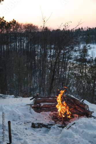 Plakat Ognisko pali w śniegu w leśnym wzgórzu, na tle ośnieżonych drzew i gór ognisko płonące w zimnej zimie. nocny ogień i namiot. Turystyka piesza. Płomienie, pionowe, tło