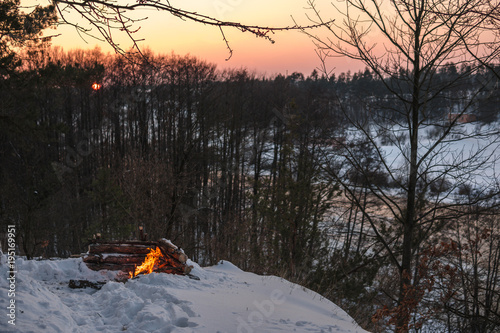 Plakat Ognisko pali w śniegu w leśnym wzgórzu, na tle ośnieżonych drzew i gór ognisko płonące w zimnej zimie. nocny ogień i namiot. Turystyka piesza. Płomienie, tło
