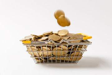 Wall Mural - Metal grocery basket for shopping in supermarket with lowered yellow handles with the coins falling into it isolated on white background. Concept of shopping, money. Copy space for advertisement