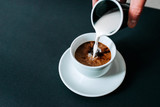 Pouring milk in black coffee. Isolated background.