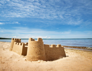 Poster - Sandcastle on the sea in summertime. Seashore on beautiful day. Sand on the beach and blue water