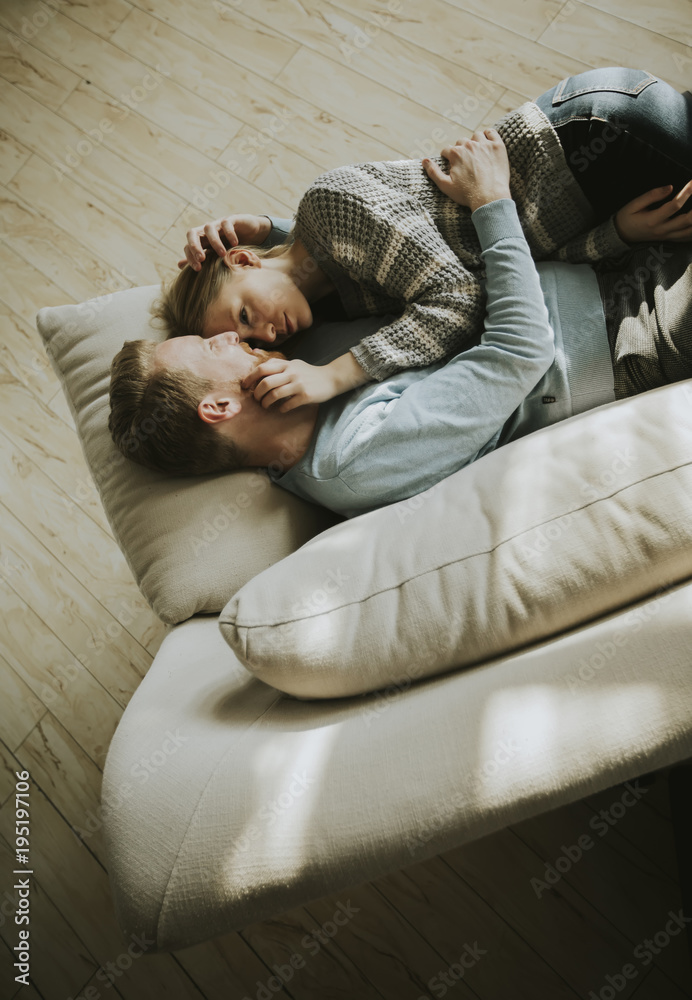 Loving couple lying down on the sofa in the room - obrazy, fototapety, plakaty 