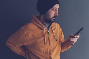 Wall Mural - Casual adult male with cap looking at mobile phone