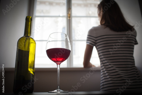Fotografie, Obraz Woman looking out her window in a dark room drinking glass of wine