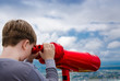 the boy holds in his hands and looks at the city through a big red binoculars
