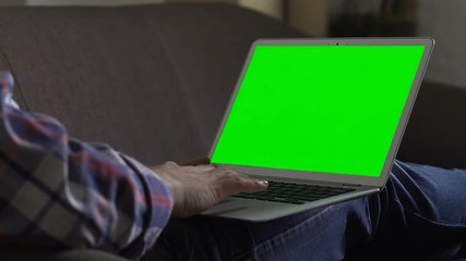 Male freelancer sitting on couch with laptop, surfing internet in free time