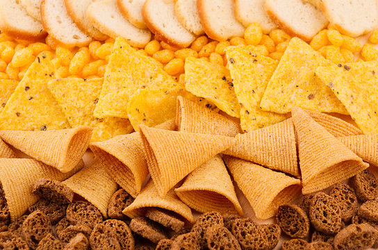 Assortment crunchy snacks - popcorn, nachos, croutons, corn sticks, potato chips as decorative background, top view, closeup.