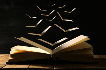 image of open antique book over wooden table with flying pages.