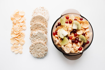 crisp bread and delicious crispy cornflakes with kiwi and cranberries in bowl over white background,  healthy breakfast