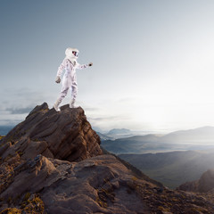 Wall Mural - Portrait of astronaut in a space suit. Futuristic astronaut on the planet, standing on top of a mountain and stretches his hand away