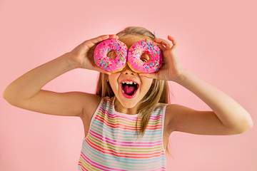 young beautiful happy and excited blond girl 8 or 9 years old holding two donuts on her eyes looking through them playing cheerful