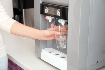 Woman filling glass from water cooler in office