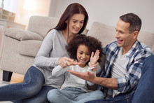 Inspired Family. Pretty Inspired Curly-haired Smiling And Having Fun With Her Parents While They All Sitting On The Floor