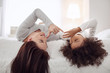 Entertaining. Pretty cheerful curly-haired girl smiling and lying with her mother on bed and they having fun