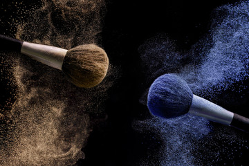 Two brushes for makeup with brown and blue make-up shadows in motion on a black background.