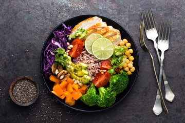 Wall Mural - Buddha bowl dish with chicken fillet, brown rice, avocado, pepper, tomato, broccoli, red cabbage, chickpea, fresh lettuce salad, pine nuts and walnuts. Healthy balanced eating. Top view