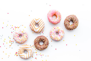 Wall Mural - Donuts decorated icing and sprinkles on white background top view copy space pattern