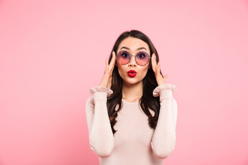 Poster - Photo of beautiful adult girl with long dark hair in round glasses expressing excitement, isolated over pink background