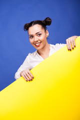 Happy woman holding a yellow banner in hands over blue background in studio photo