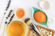 Bright egg yolks, oatflakes, honey, lavender with cosmetic brush closeup, natural holistic ingredients for homemade beauty care. Fresh products for glowing skin. White background viewed above. 