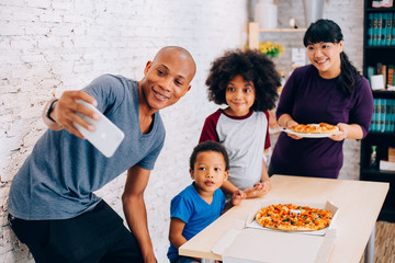 Happy parents and little boy and girl having a meal and taking selfie by smartphone at home. Family and parenthood concept