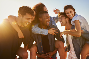 group of friends on vacation having piggyback race on beach
