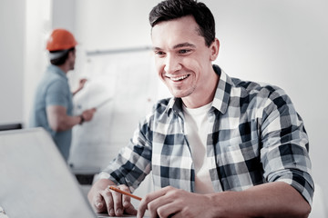 Sticker - Keep smiling. Handsome worker holding elbows on the table and expressing positivity while looking at computer