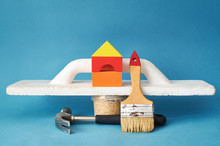The Concept Of Renovation In The Apartment. A Spatula, A Hammer And A Toy House.