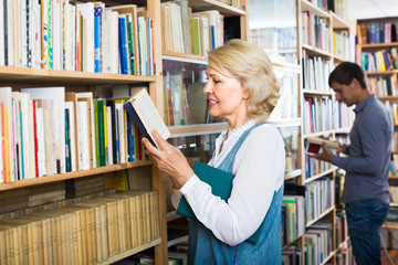 Wall Mural - mature woman with book among bookshelves .