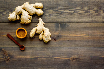 Spice and condiment. Ground ginger in small bowl near ginger root on dark wooden background top view copy space