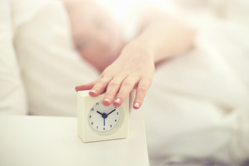 Wall Mural - close up of woman with alarm clock in bed at home