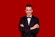 © Svetlana - Portrait of smiling handsome stylish man in elegant black suit on red background. Business style. Fashionable image. Office worker. Sexy man standing and looking at the camera