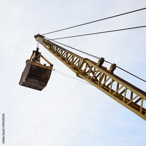Fotografia, Obraz Old yellow mechanical clamshell grab on blue sky background