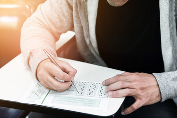 Wall Mural - Student holding pencil writing on paper answer sheet.sitting on chair doing final exam attending in examination on classroom.